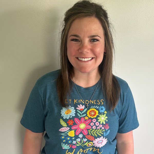 Smiling woman wearing a blue floral shirt with 'Let Kindness Bloom' text.
