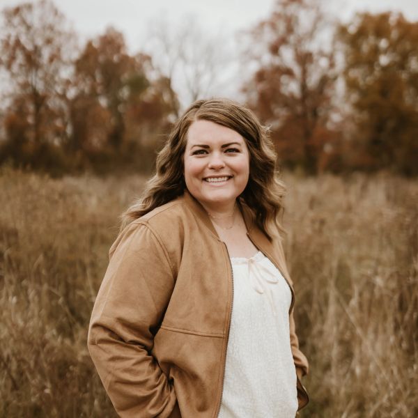 Woman smiling in a brown jacket outdoors.