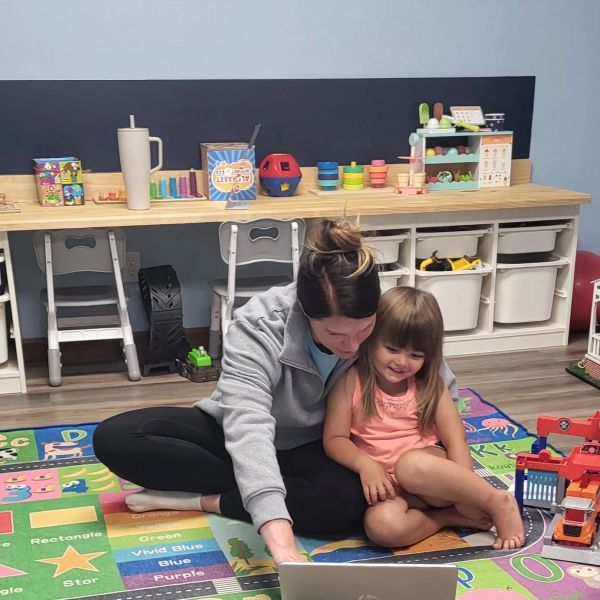 Woman and child sitting on colorful mat with a laptop.