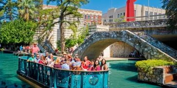 People enjoying a boat ride on a river with a stone bridge and sculpture.