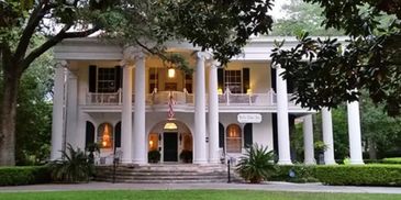 Elegant white mansion with tall columns and lush greenery.