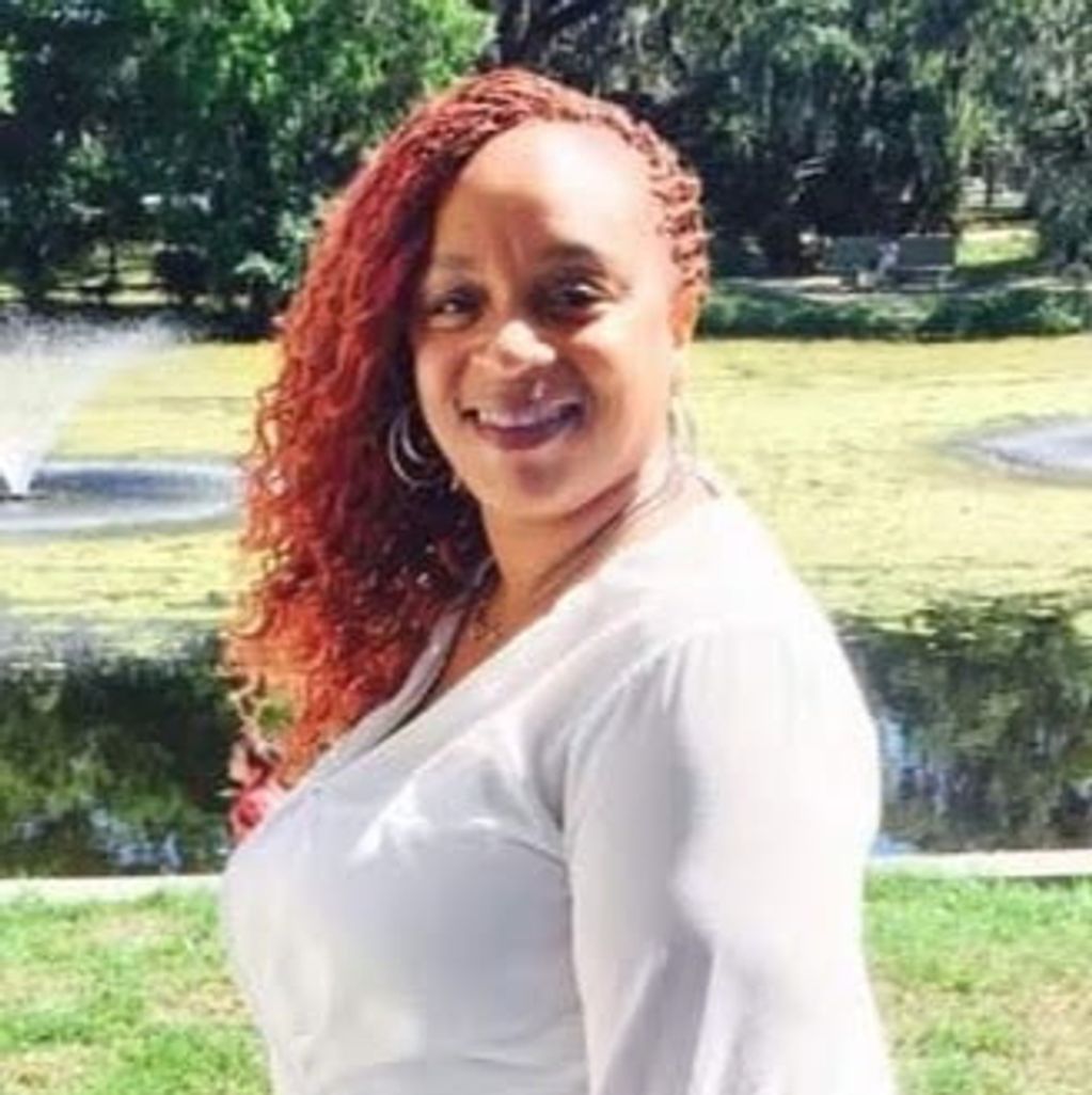 Woman with red curly hair smiling in a park near a pond with fountains.