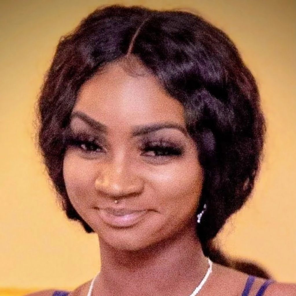 Woman in a blue dress smiling with a white necklace.