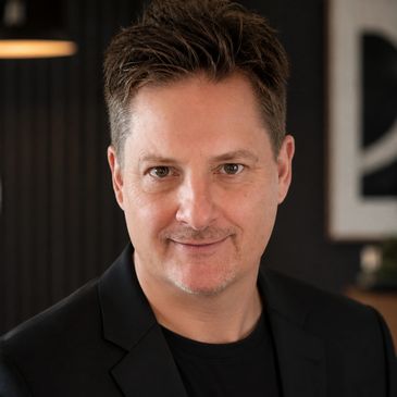 Professional headshot of a confident man in a black blazer.