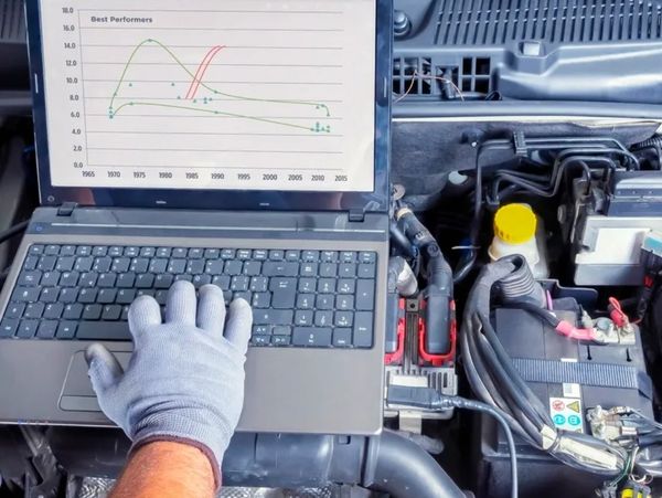 Technician using a laptop to diagnose a car engine issue.