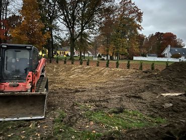 Bulldozer clearing a backyard with autumn trees and houses in the background.