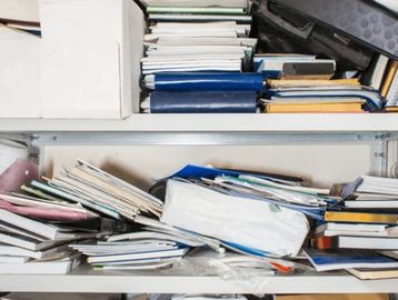 A cluttered shelf filled with disorganized books and folders.