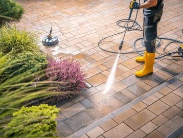 Person power washing a patio with yellow boots and gloves.
