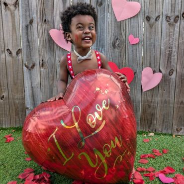 Happy toddler holding a heart-shaped balloon that says "I Love You".