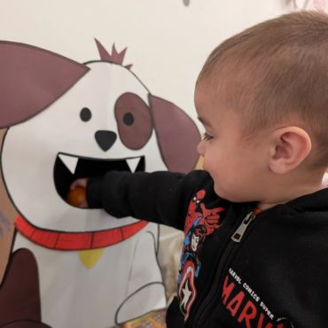 Toddler placing hand in cartoon dog's mouth on wall.