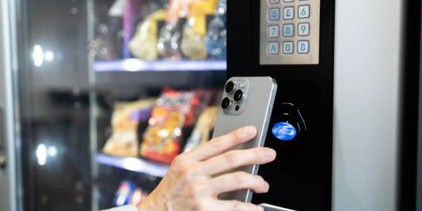A person uses a smartphone to make a contactless payment at a vending machine.