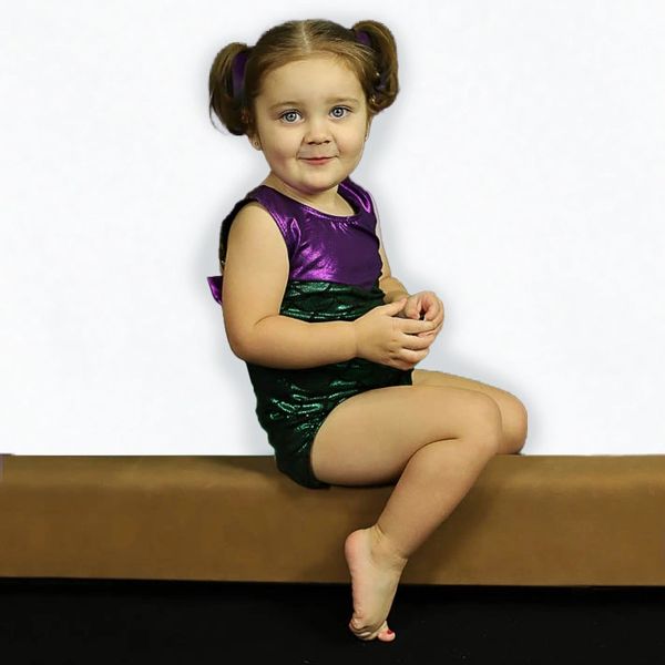 Little girl in a purple and green outfit sitting and smiling.