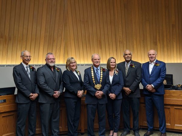 Group of seven formally dressed individuals posing indoors with one wearing a mayoral chain.