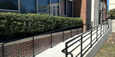 Wheelchair accessible ramp with black handrails beside a brick building.