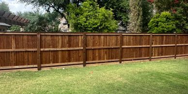 A wooden fence encloses a green backyard with trees in the background.