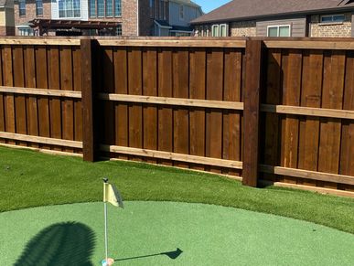 Small backyard putting green with a wooden fence and houses in the background.