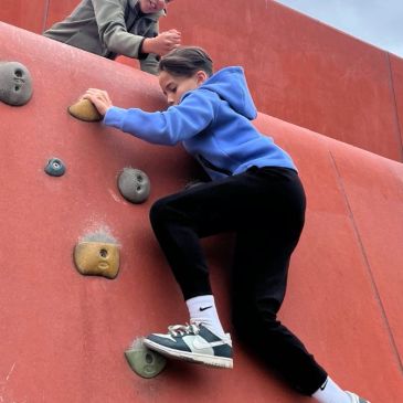 Child climbing a red rock climbing wall.