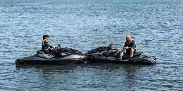 2 people on Jetskis in the middle of water resting and having a conversation.