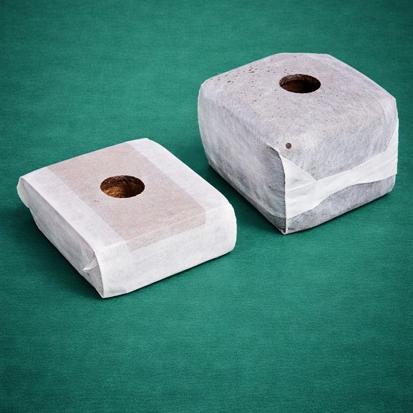 Two wrapped soil blocks with central holes on a green surface.
