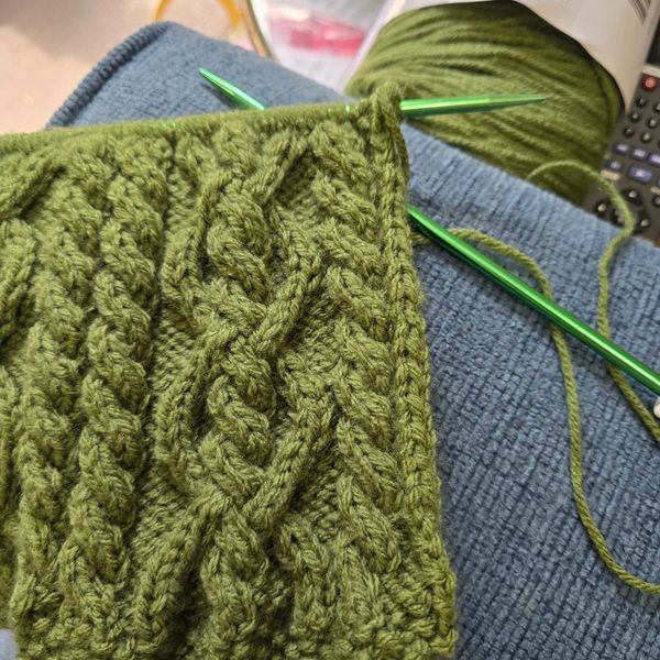 Green yarn knitting in progress with cable patterns.