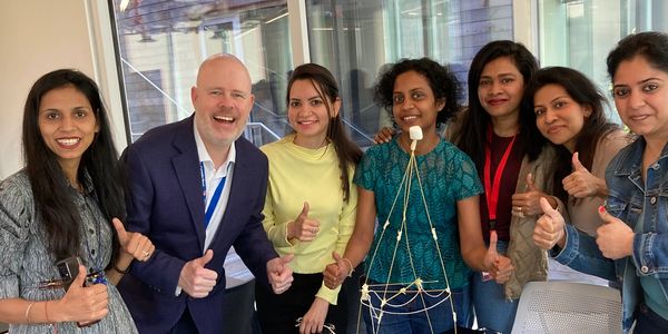 Group of seven people smiling and giving thumbs up around a table with a marshmallow tower.
