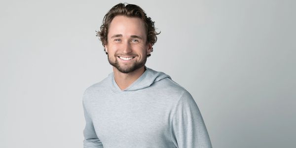 Smiling man in a light gray hoodie against a plain background.
