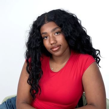 Young woman with long black curly hair in a red top.