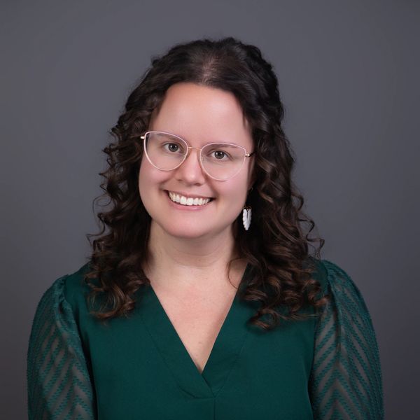 Smiling woman with glasses and curly hair in a green top.