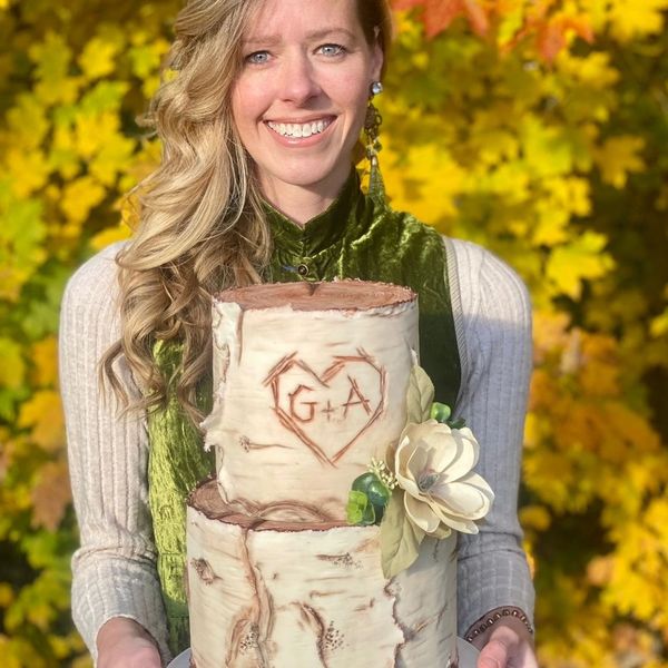 A woman holding a birch bark cake with carved initials and a flower.