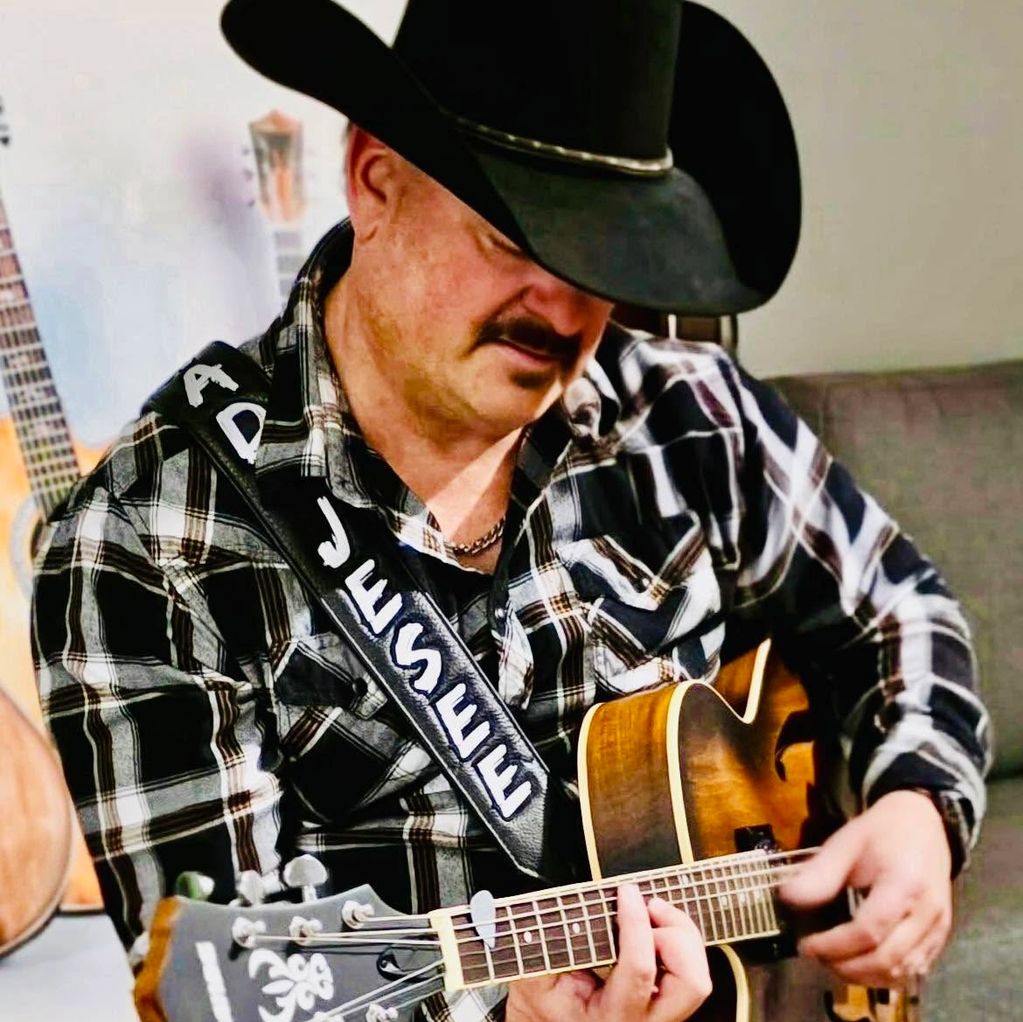 Man in cowboy hat playing guitar with personalized strap.
