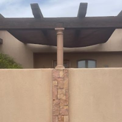 Desert-style patio with stone and stucco wall under a wooden pergola.