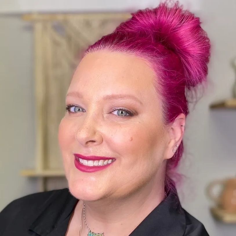 Woman with vibrant magenta hair styled in a bun, smiling warmly.