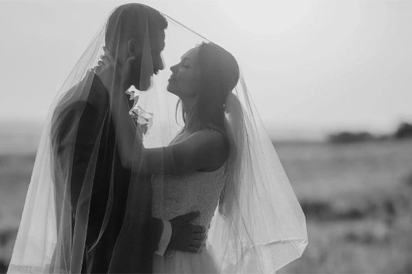 A bride and groom share an intimate moment under a veil outdoors.
