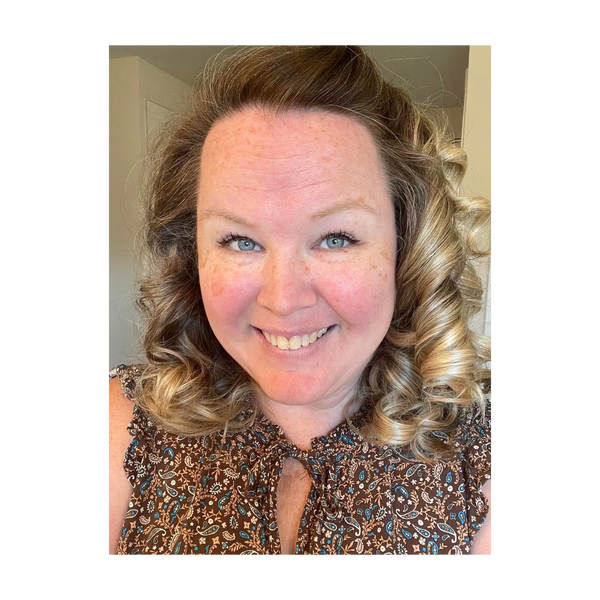Smiling woman with curly blonde hair and a patterned blouse.