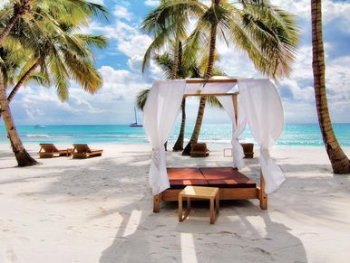 Beachside canopy bed with white curtains on a tropical sandy beach.