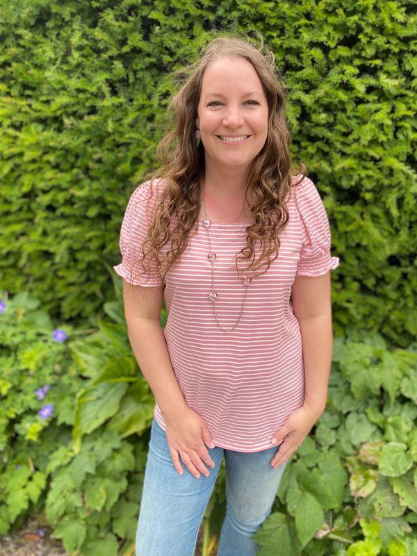 Smiling woman in pink striped shirt and blue jeans outdoors.