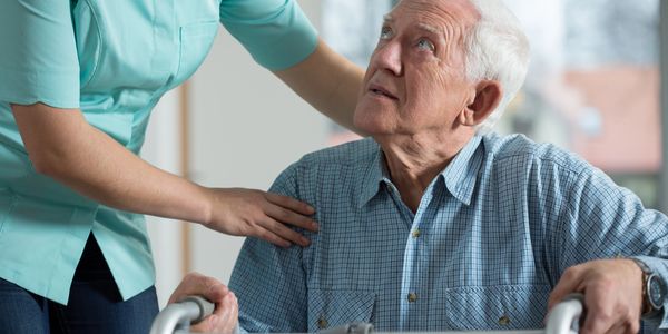 Caregiver comforting elderly man using a walker.