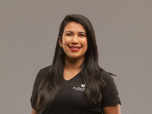 Smiling woman with long black hair wearing a black shirt against a gray background.