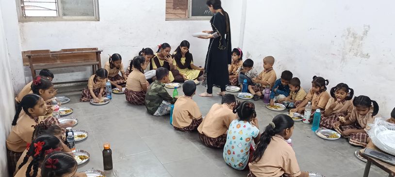 School children sitting on the floor eating their meals in a classroom.