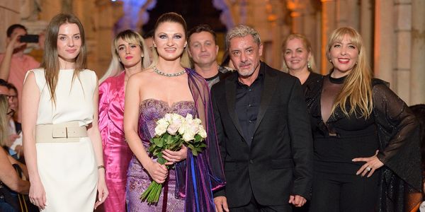 Elegant, purple, party dress worn by Angelina Jordan; surrounded by other fashion designers at show.