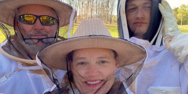 Three people in beekeeping suits smiling outdoors.