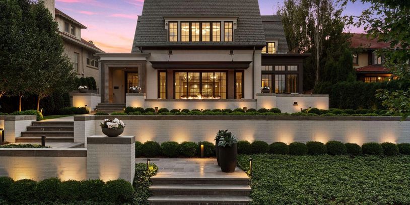 Elegant modern house with illuminated exterior and lush landscaping at sunset.