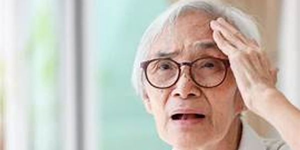 Elderly woman looking distressed and holding her forehead.