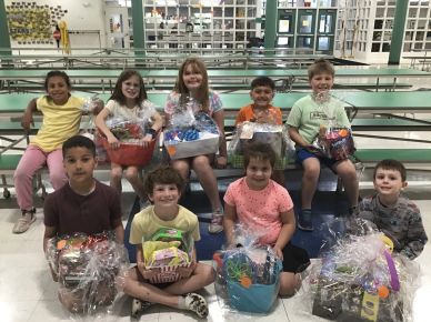 Group of children holding gift baskets in a school cafeteria.
