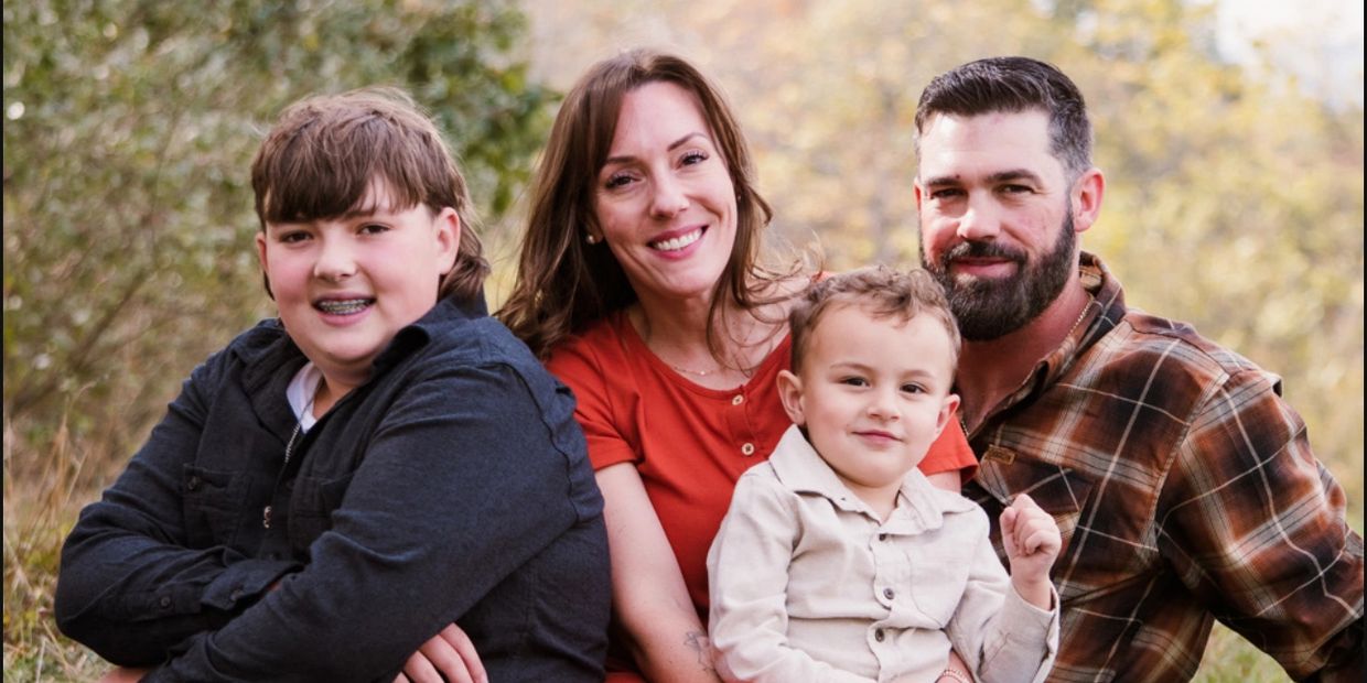 A family of four sitting on grass outdoors, smiling at the camera.