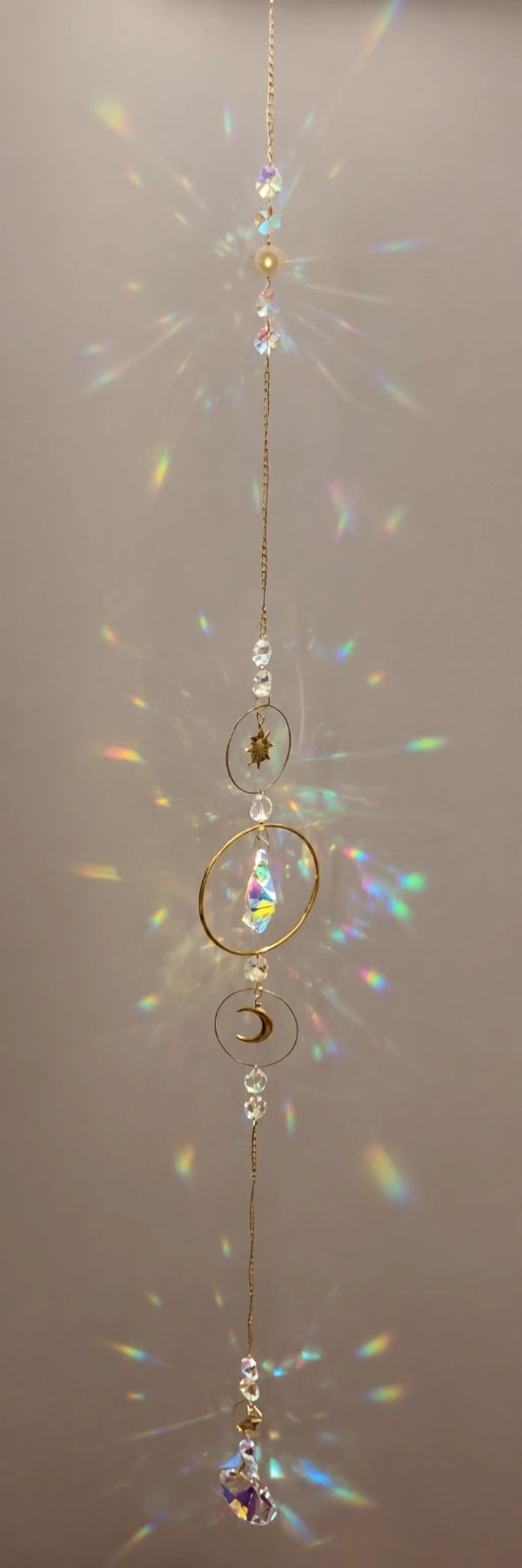 Hanging crystal suncatcher with celestial charms casting colorful light reflections.