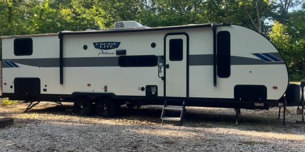 White and black travel trailer parked in a wooded area.