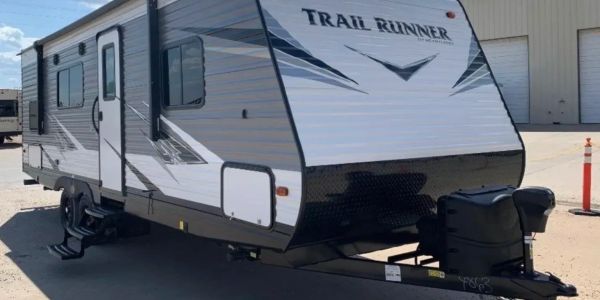 White and gray Trail Runner travel trailer parked outside.