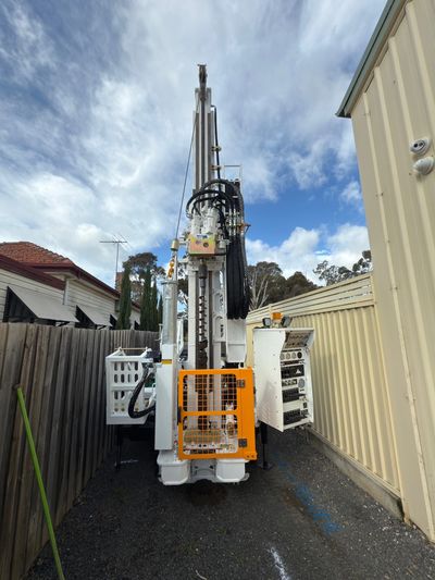 Large drilling machine positioned between two buildings under a cloudy sky.