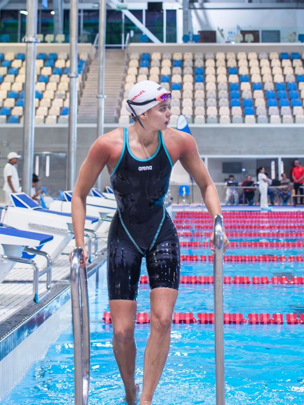 Swimmer in black suit exiting the pool at a competitive swimming venue.